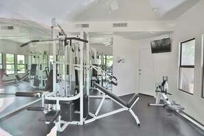 A gym with various exercise equipment, a television on the wall, and large windows.