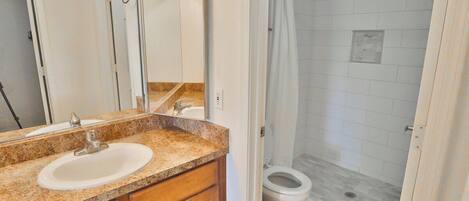 A bathroom with a sink, mirror, and shower area.
