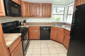 A kitchen with wooden cabinets, a black microwave, a stove, a dishwasher, and a refrigerator. - Catalina Foothills Condo on the Golf Course (Tucson)