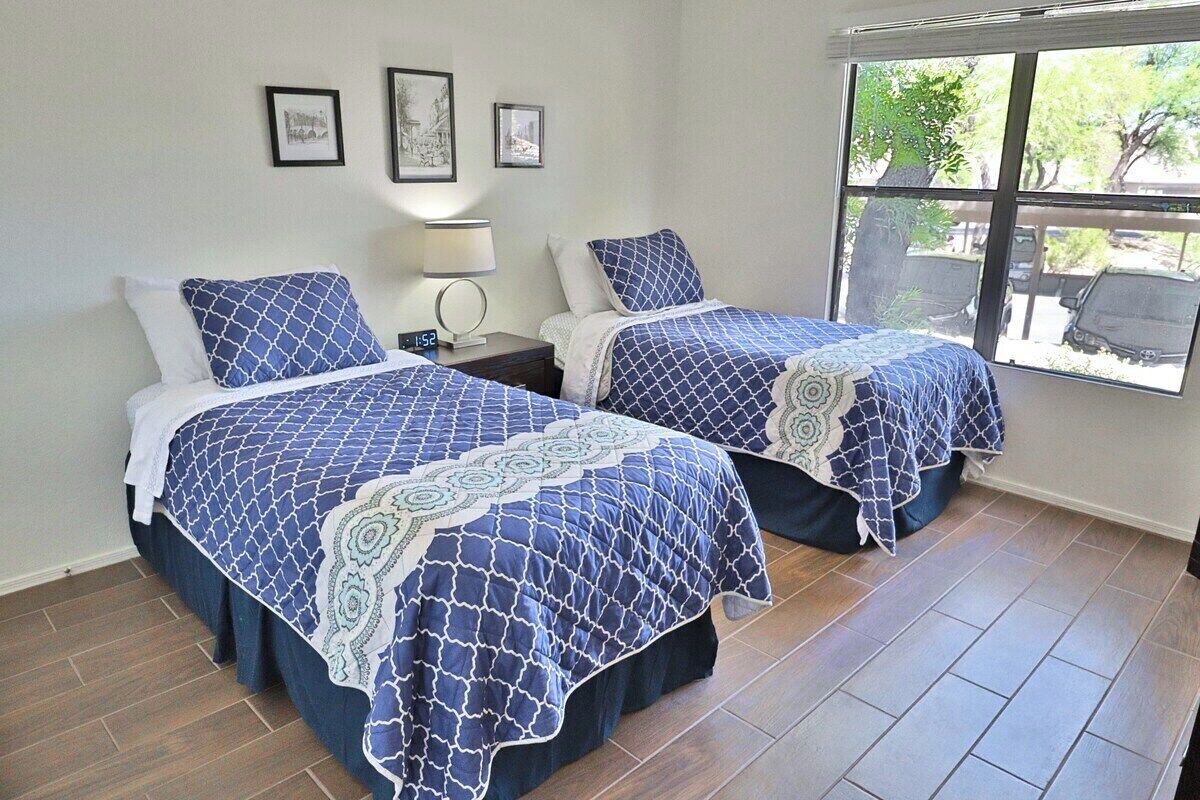 Habitación de hotel con dos camas, una mesita de noche con lámpara y ventana con vistas al exterior.