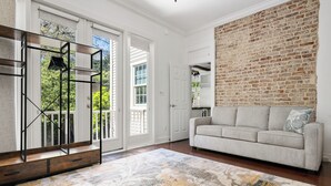 Un salon spacieux avec une grande fenêtre, un canapé blanc, un tapis à motifs et un mur en briques.