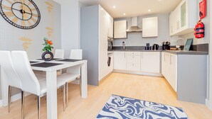 A modern kitchen with white cabinets, a black countertop, and a built-in oven. There is a dining area with a white table and chairs, and a blue patterned rug on the floor. - Modern 2-Bedroom Apartment in Central Basingstoke  walk to Festival Place & The Avil Theatre . (Basingstoke)