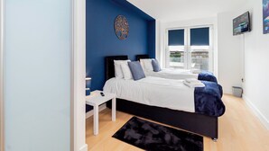 A bedroom with two beds, a white nightstand, a black rug, and a ceiling light. - Modern 2-Bedroom Apartment in Central Basingstoke  walk to Festival Place & The Avil Theatre . (Basingstoke)