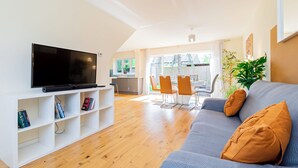 A modern living room with a flat-screen TV, a grey sofa with orange cushions, and a wooden floor. - 4-Bed Haven in Fawley – Ideal for extended stays, work trips, or family getaways. Spacious, fully furnished, and well-equipped for comfort and convenience. Your perfect home away from home. (Totton)