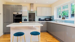 A modern kitchen with grey cabinets, a white island, and two blue bar stools. - 4-Bed Haven in Fawley – Ideal for extended stays, work trips, or family getaways. Spacious, fully furnished, and well-equipped for comfort and convenience. Your perfect home away from home. (Totton)