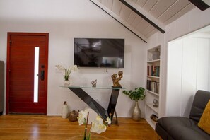 A living room with a red door, a mounted TV, a glass console table, and a bookshelf. - Dreamy Farmhouse In Studio City (North Hollywood)