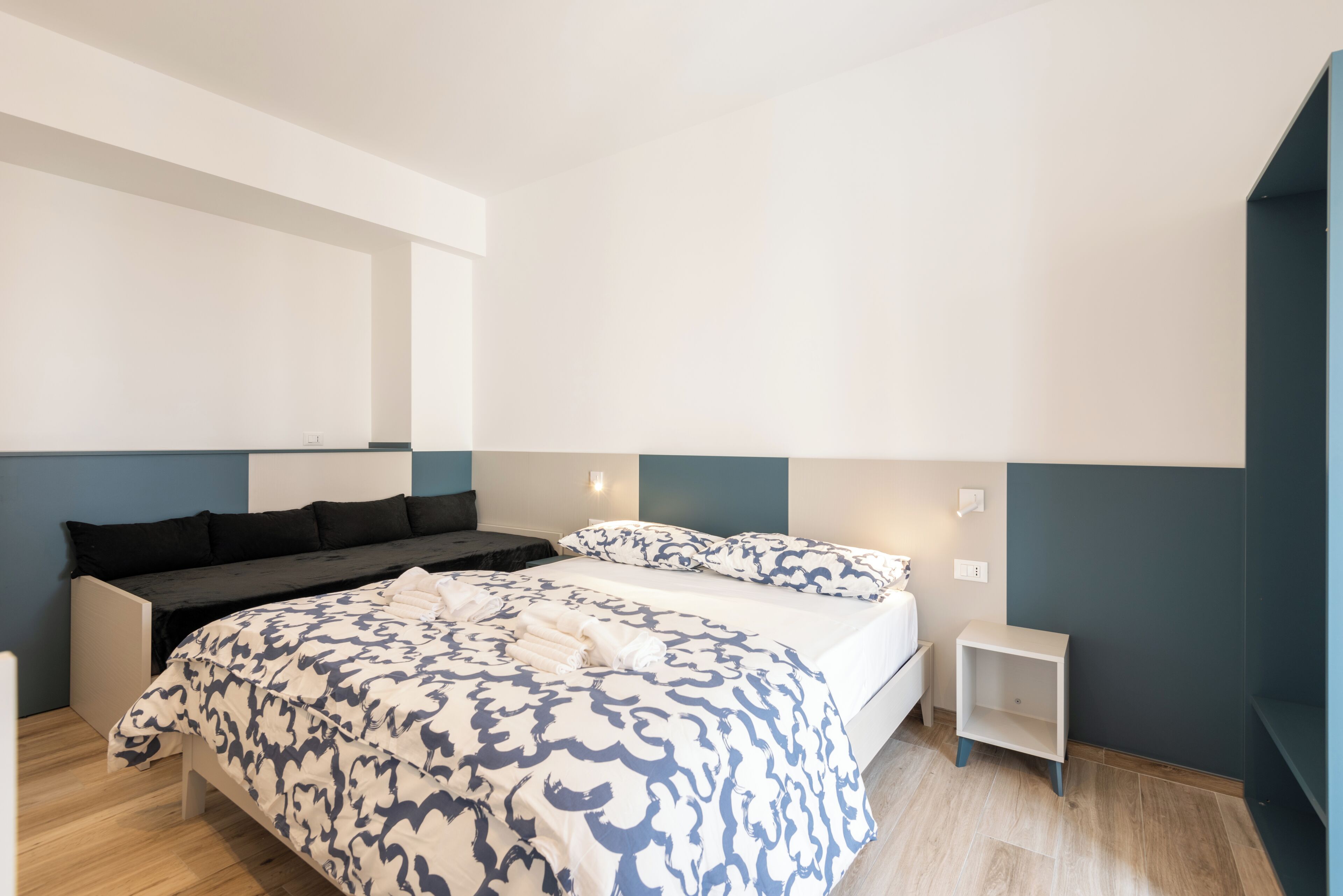 A modern bedroom with a large bed, a sofa bed, and a small bedside table.