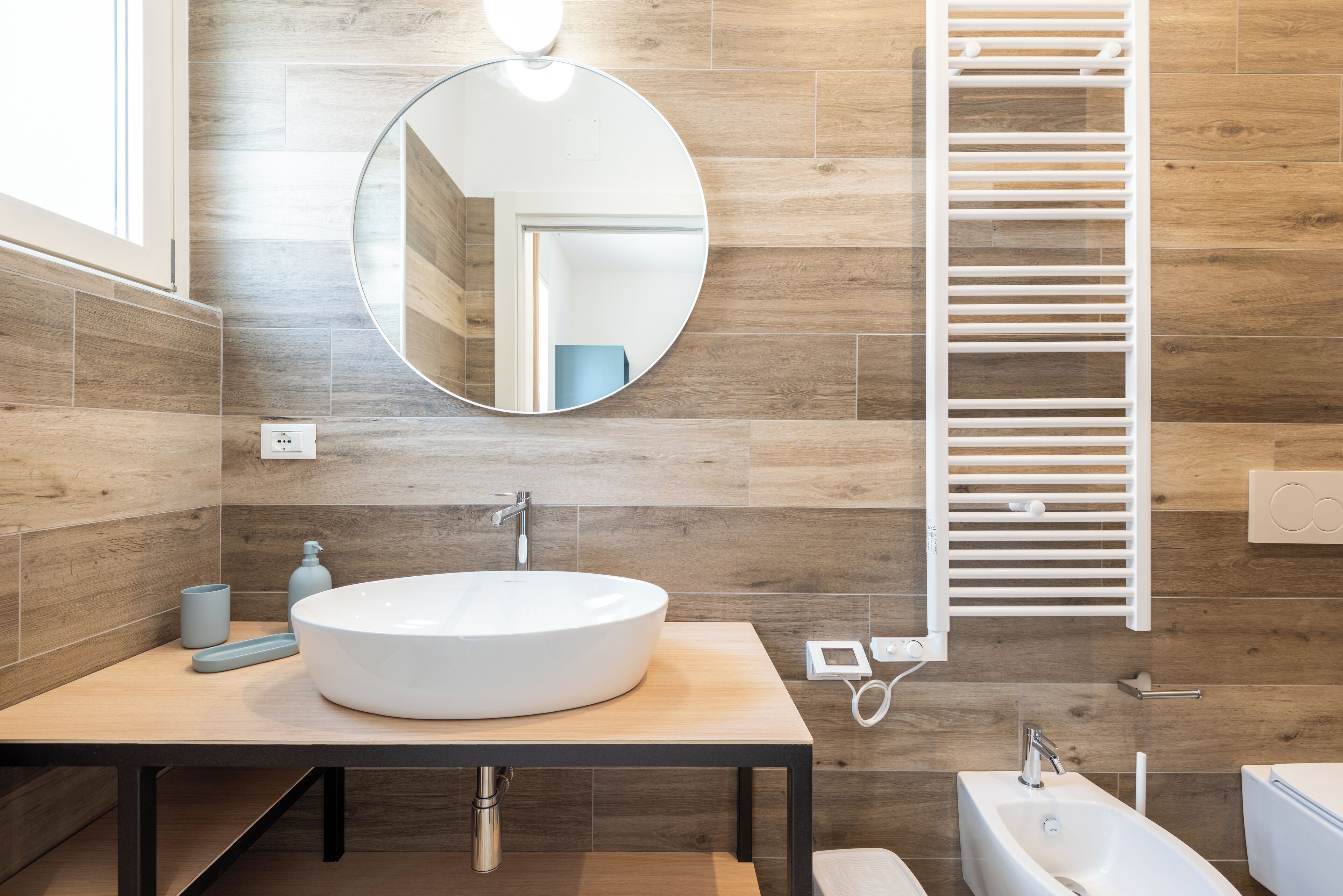 Un baño moderno con un espejo redondo, dos lavamanos, un perchero para toallas y un inodoro.