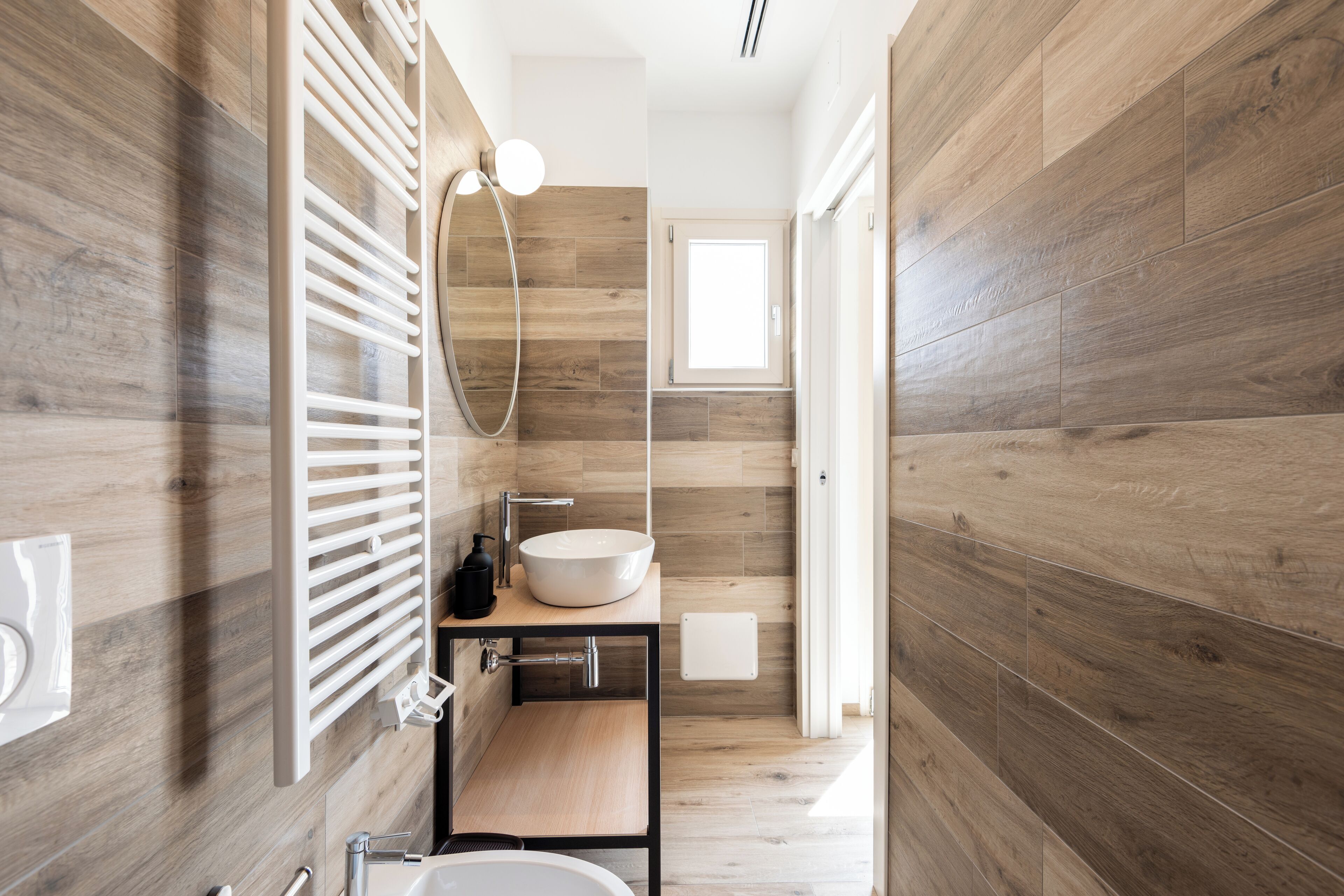 A modern bathroom with a wooden floor, a freestanding sink, and a wall-mounted towel rack.
