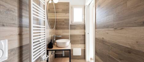 A modern bathroom with a wooden floor, a freestanding sink, and a wall-mounted towel rack.