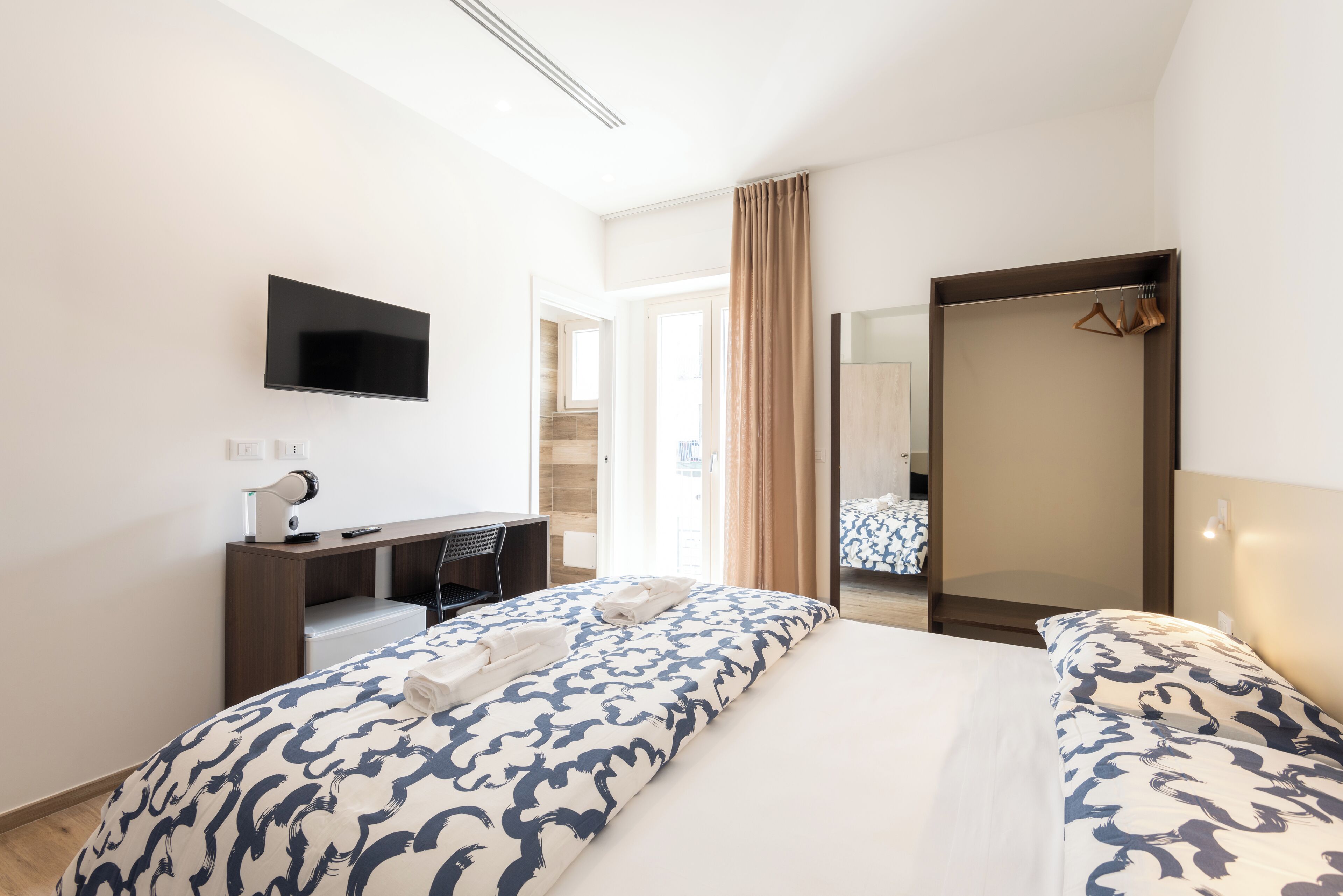 Ein Hotelzimmer mit Bett, Schreibtisch, Stuhl, Fernseher und Spiegel.