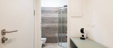 A bathroom with a shower, toilet, and a coffee machine on the counter.