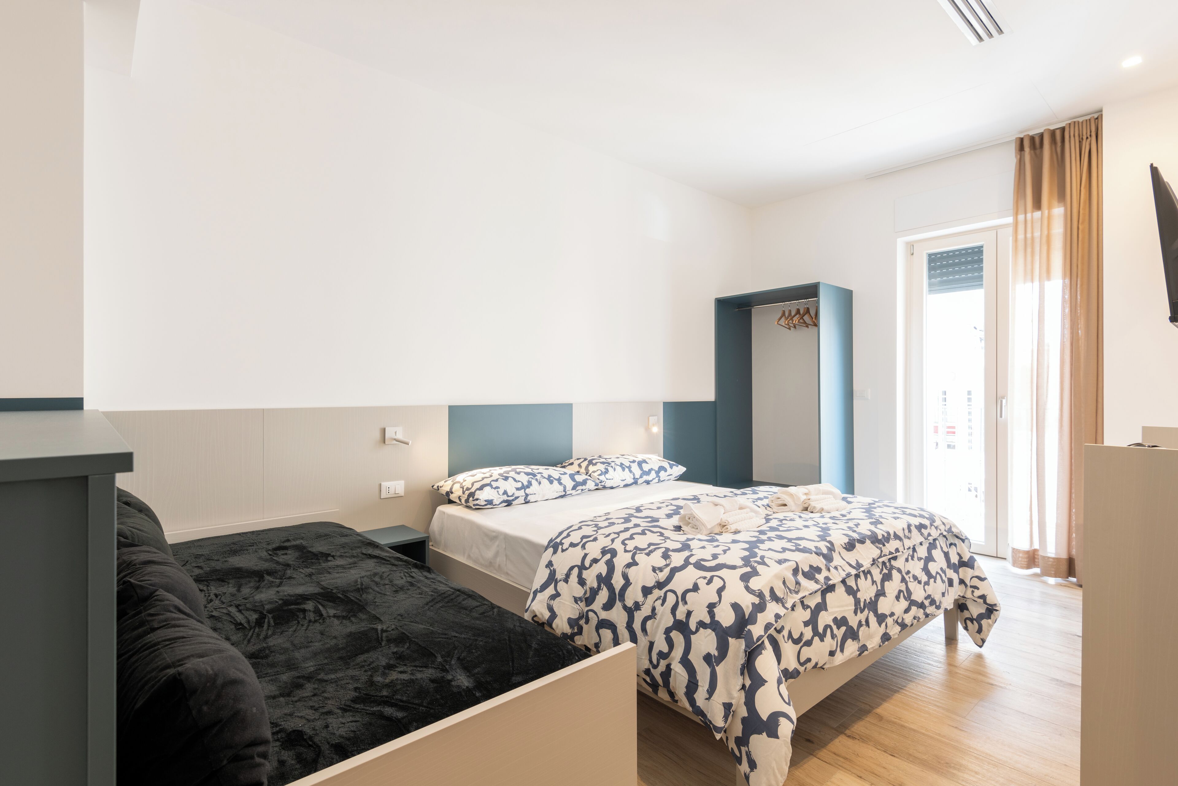 A hotel room with a bed, a small desk, a chair, a wardrobe, and a mirror.