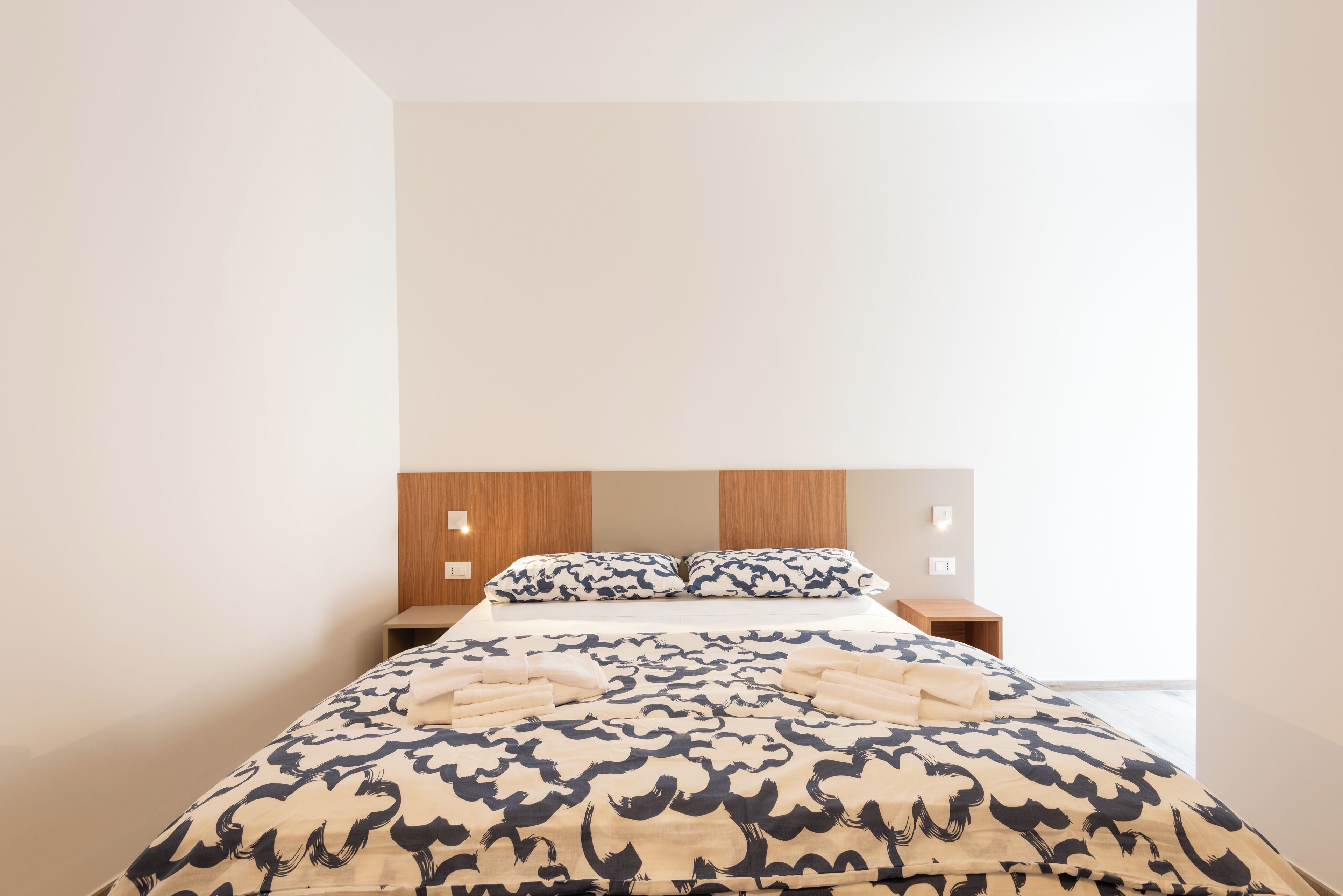 Quarto de hotel moderno com uma cama grande, cabeceira de madeira e vista para a cidade.