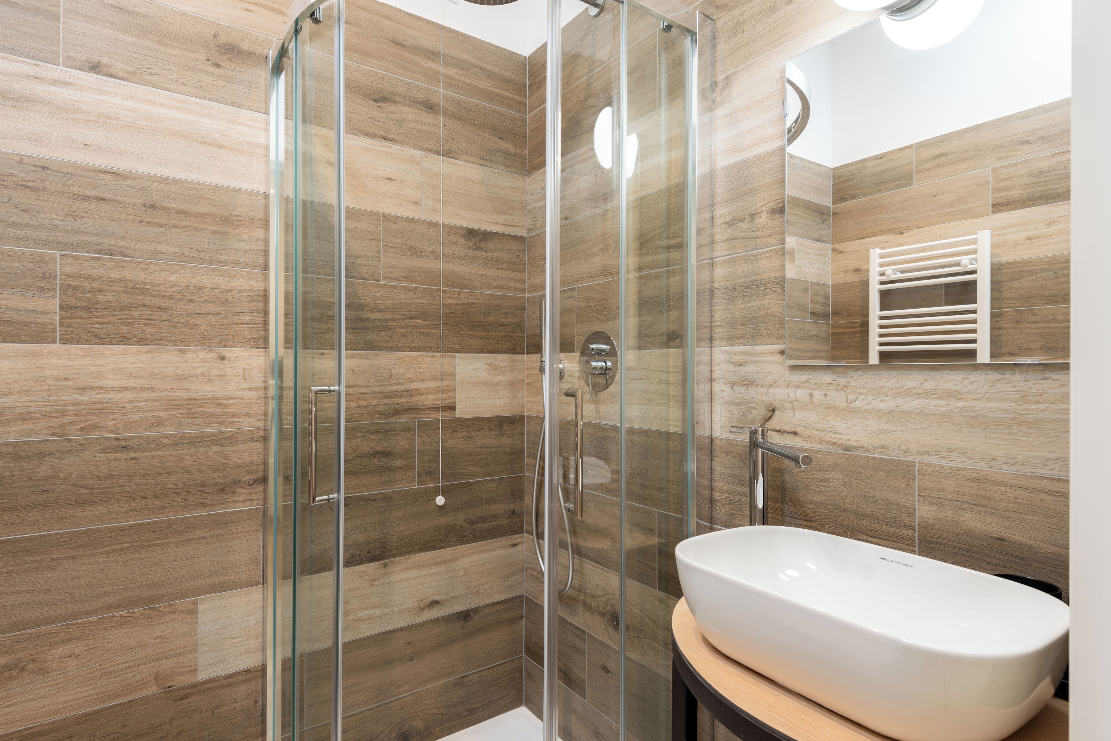 A modern bathroom with a glass shower enclosure, a white sink, and wooden wall tiles.