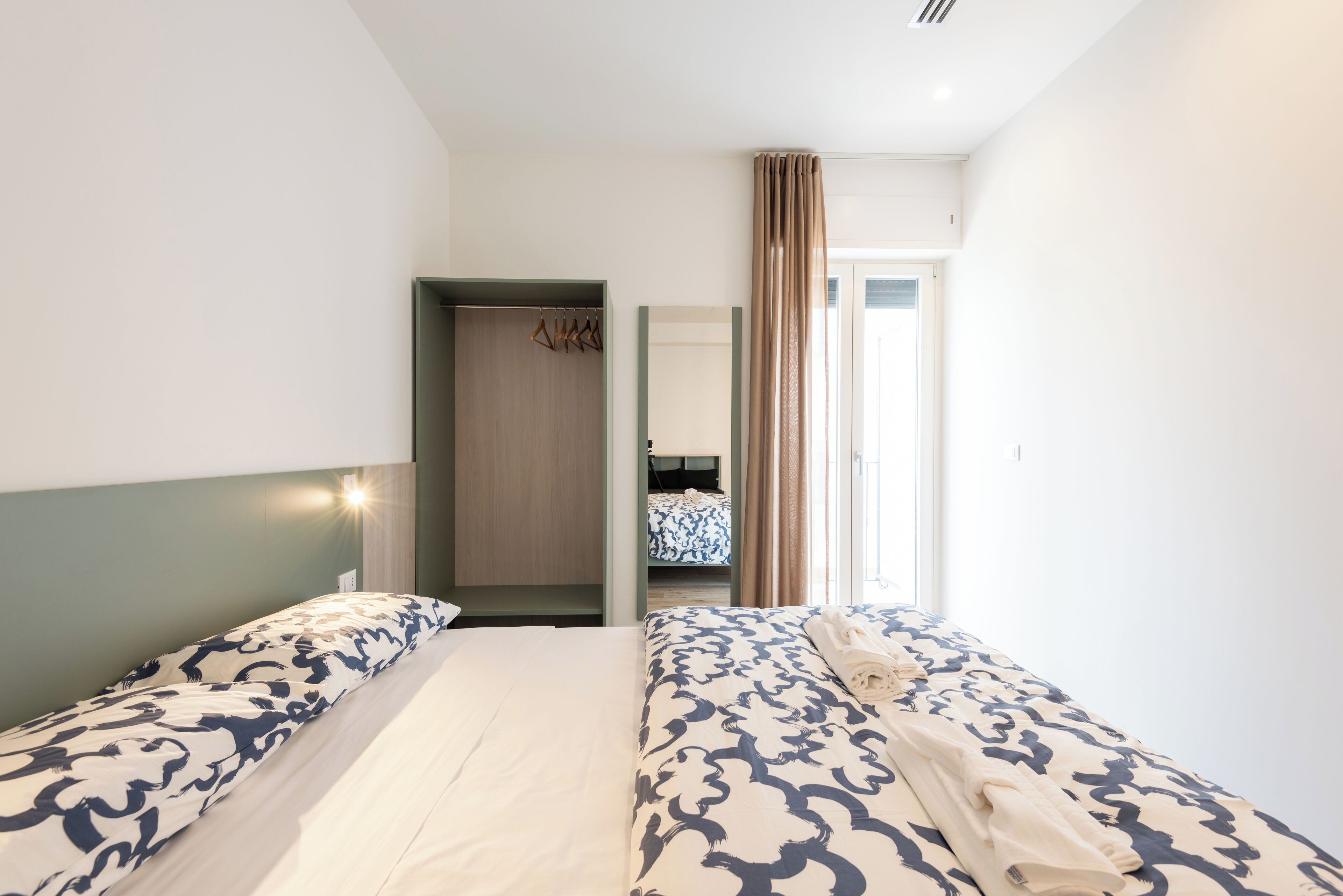 A hotel room with two beds, a wardrobe, and a bathroom visible through an open door.