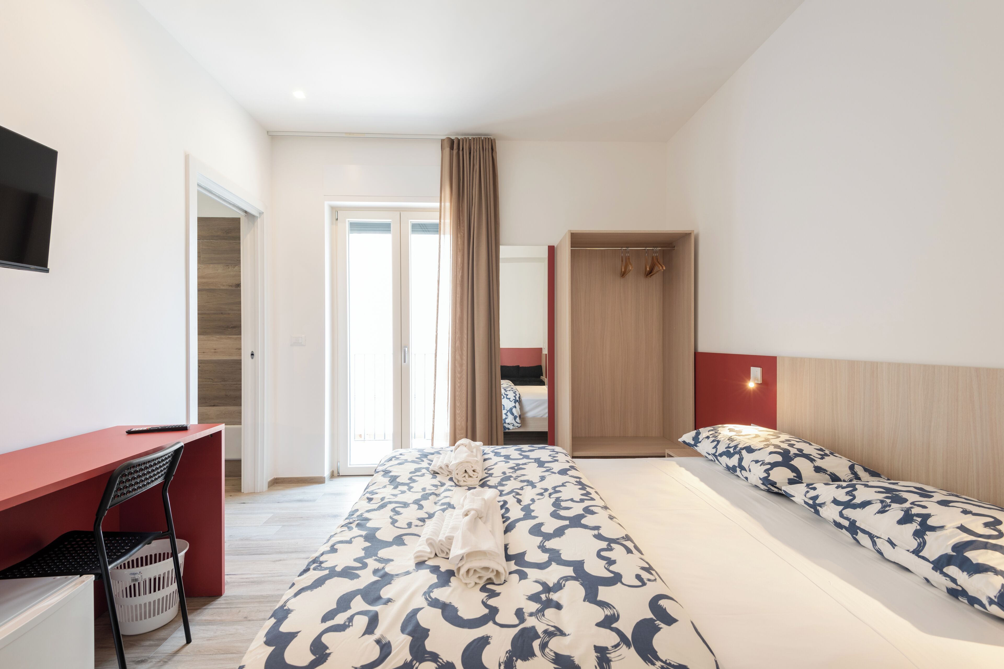 A hotel room with a desk, two beds, a TV, and a wardrobe.