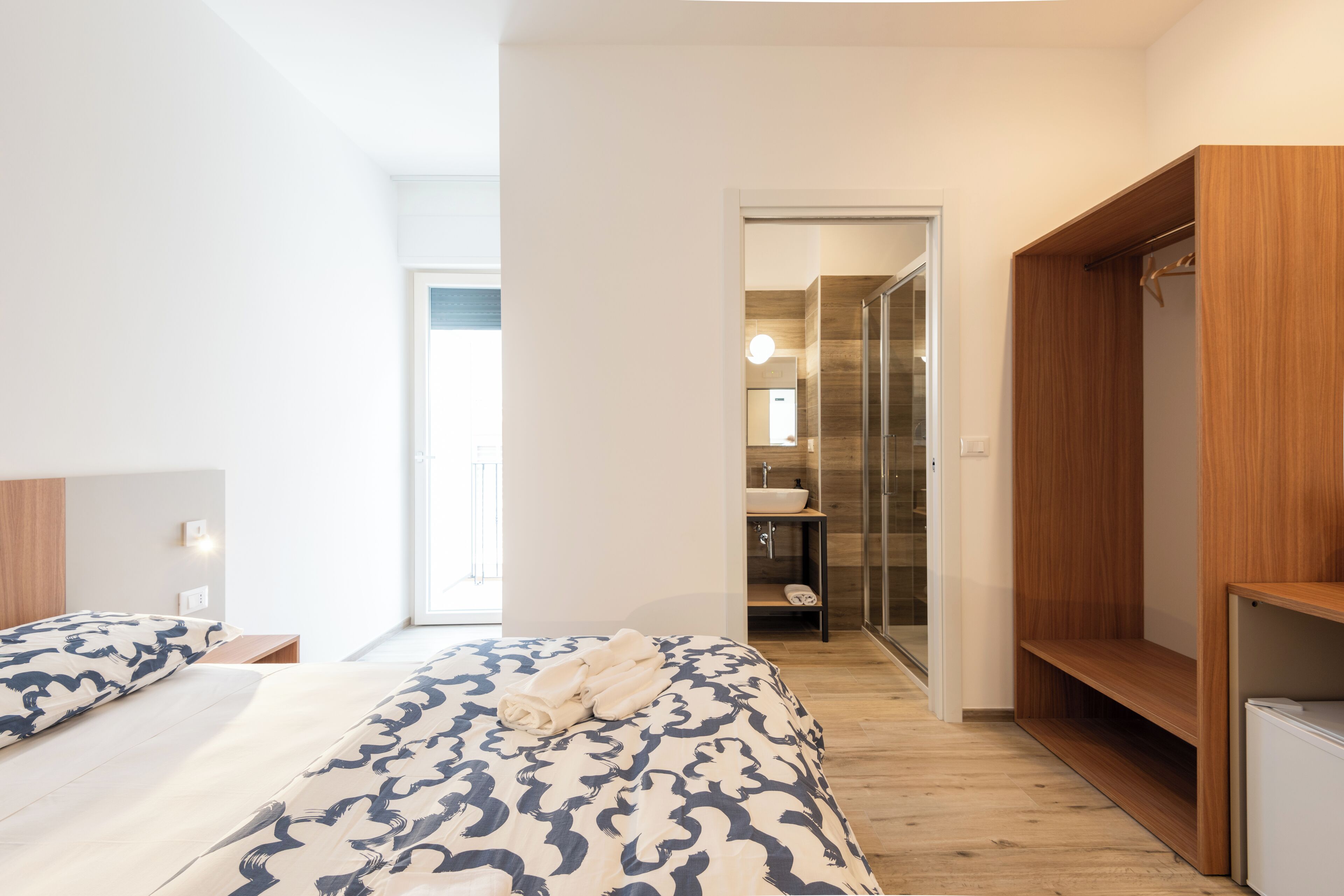 Een moderne hotelkamer met een groot bed, een houten garderobe en een badkamer die door een open deur zichtbaar is.