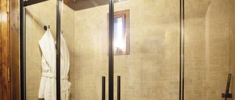 A glass-enclosed shower area with a marble floor, a wooden ceiling, and a white bathrobe hanging on the door.
