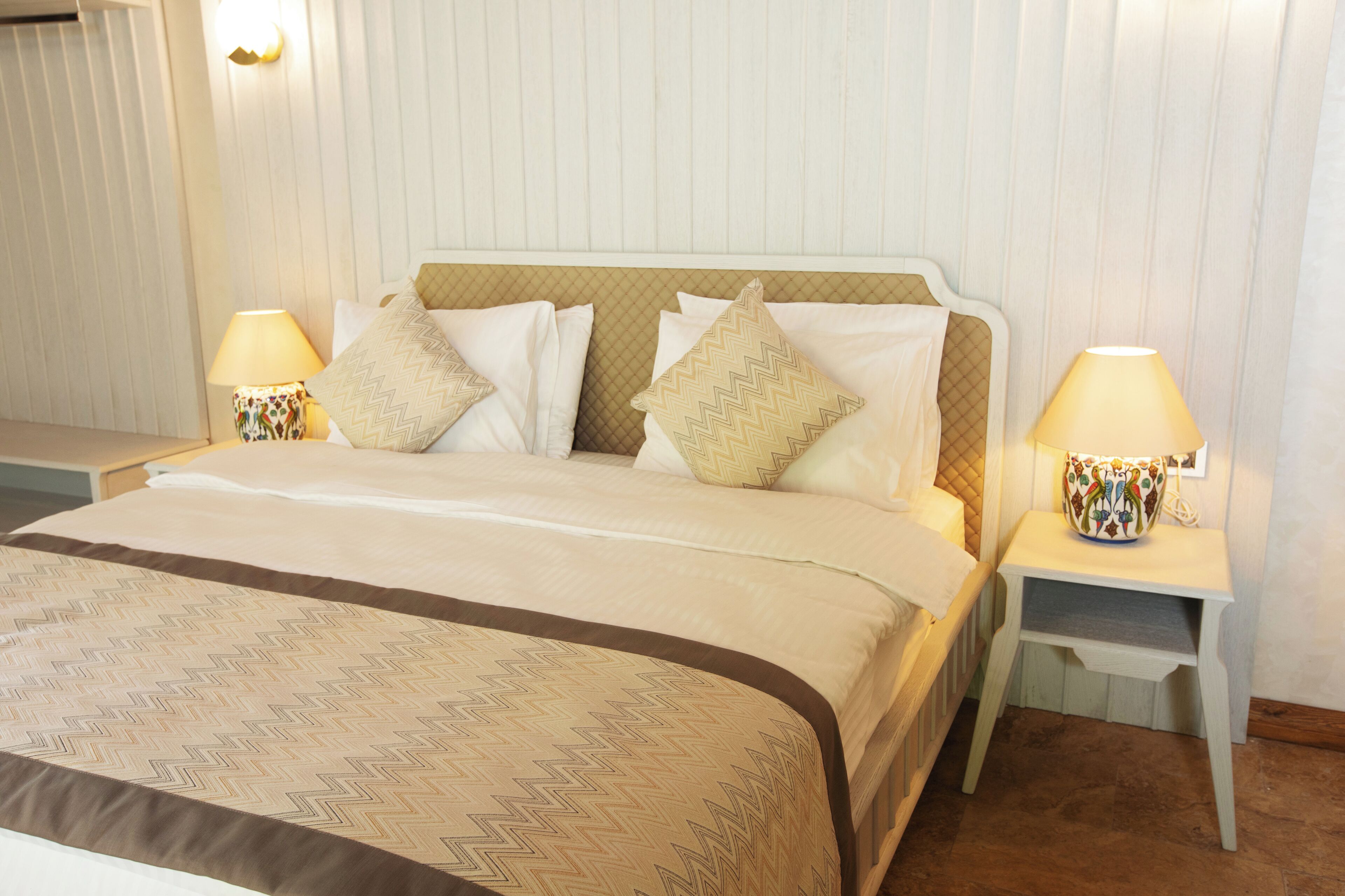 A neatly made bed with a patterned bedspread, two bedside lamps, and a headboard.