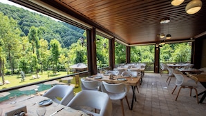 A restaurant with outdoor seating, wooden tables, white chairs, and a view of a forested hillside. - Casa Giallo Managed By Dedeman (Sapanca)