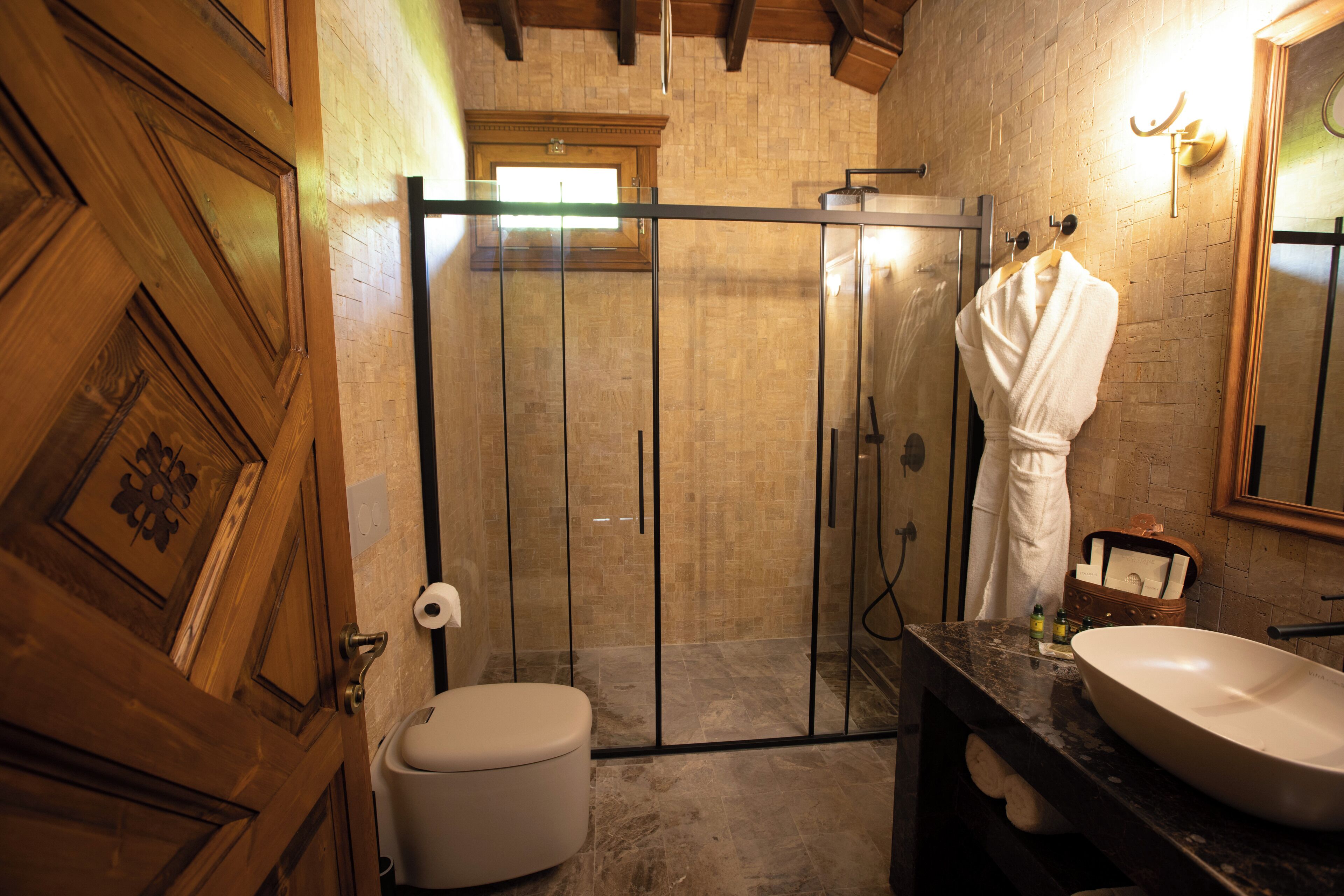 Ein Badezimmer mit Holztür, Toilette in Weiß, einer Duschkabine aus Glas, einem Marmorwaschbecken und einem Handtuchhalter.