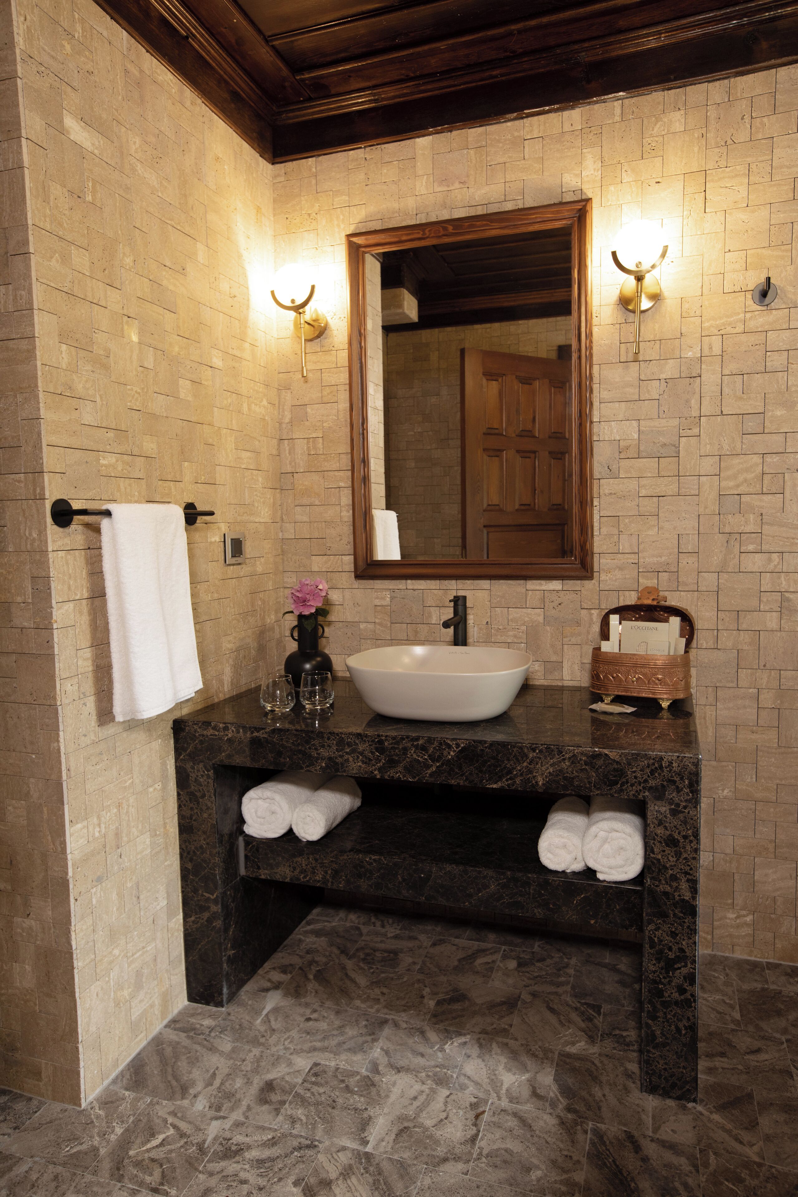 A bathroom with a marble sink, a towel rack, a mirror, and a wall-mounted light fixture.