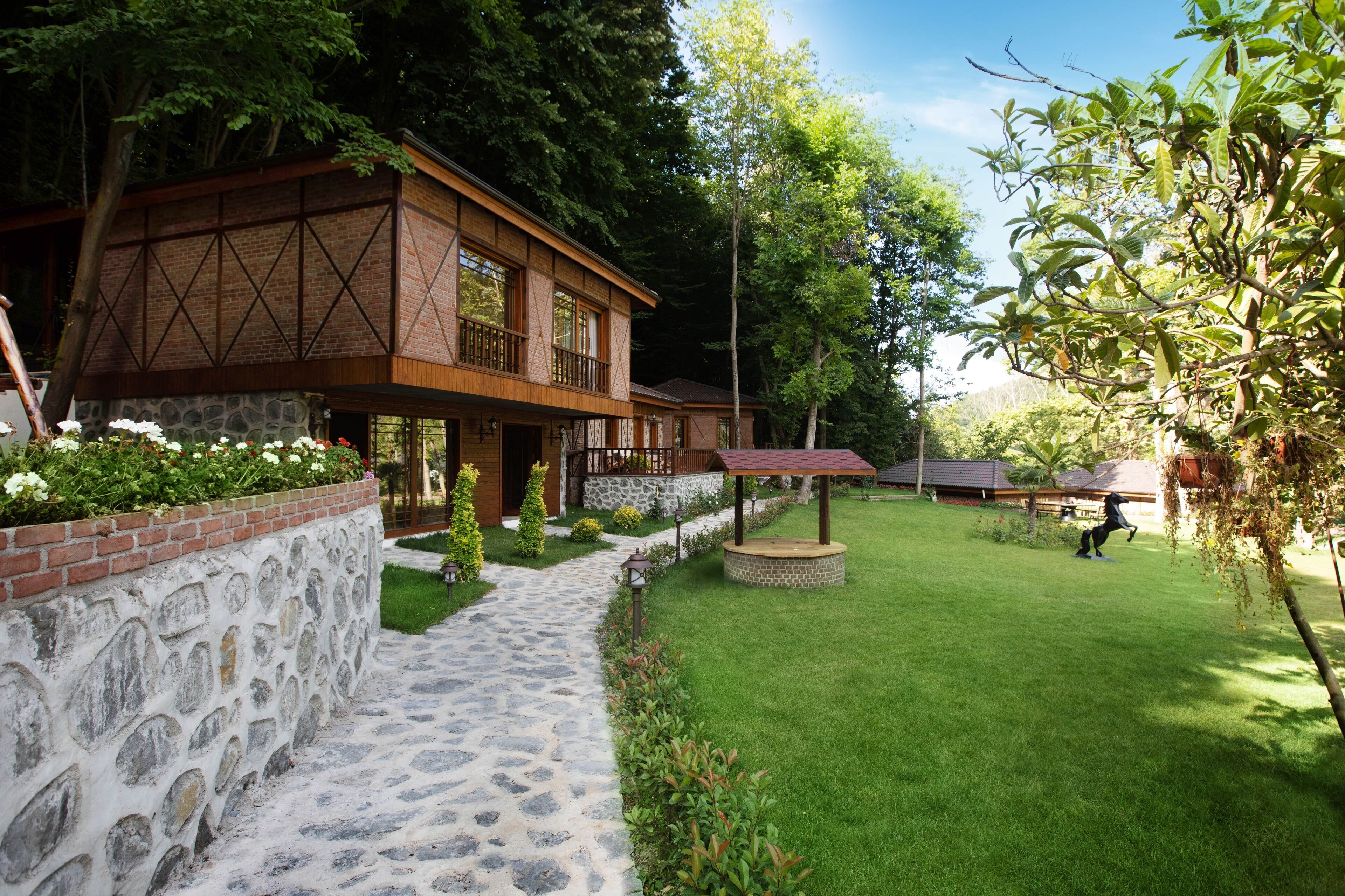 A two-story house with a stone pathway leading to the entrance, surrounded by lush greenery and a well-maintained lawn.