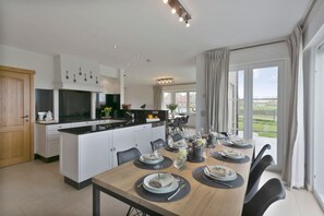 A modern kitchen with white cabinets, a wooden dining table set for six, and a large window offering a view of the outdoors. - Family House With a Beautiful View in Damme (Bruges)