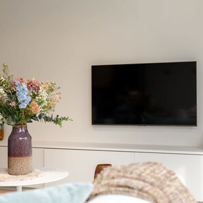Relax in this stylish living room with a flat-screen TV and a beautiful vase with fresh flowers on a round table.