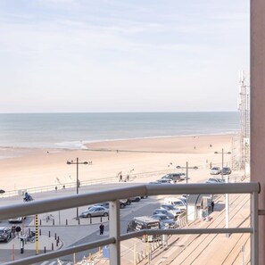 A beach view from a balcony with a parking area and a road in the foreground. - Cosy Flat With Lateral sea View (Middelkerke)