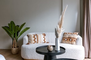 A cozy living room with a white sofa, patterned cushions, a small round table with a vase, and a potted plant. - Modern and Bright Studio in Centre of Knokke (Knokke-Heist)