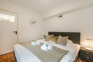 A neatly made bed with a headboard, a bedside lamp, and rolled towels on the bed. - Characterful Apartment With Lateral sea View (Middelkerke)