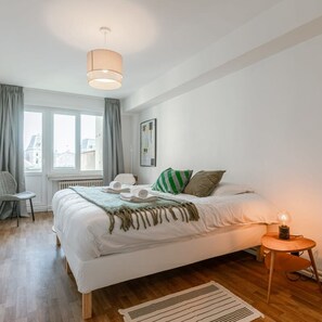 Relax in a serene bedroom with a large bed, a small table, and a lamp.