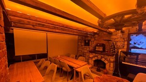 A cozy room with a stone fireplace, a wooden table, and a television displaying a news channel. - hotel budapest (Seferihisar)