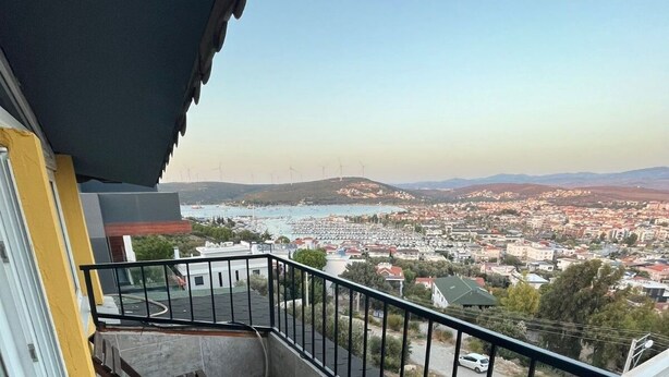 A balcony with a view of a coastal town, a wind turbine, and a clear sky. - hotel budapest (Seferihisar)