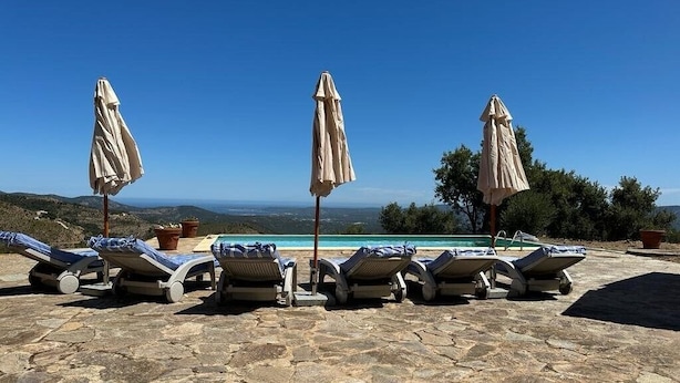 Une terrasse en pierre avec des chaises longues et des parasols, donnant sur une piscine et offrant une vue panoramique.