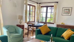Un salon chaleureux avec un canapé vert, une table basse en bois sur laquelle sont posées des boissons, et un coin repas avec une table et des chaises.