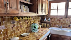 Une cuisine avec des meubles de rangement en bois, un pare-feu en carreaux et une fenêtre avec une horloge.