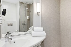Un baño moderno con un espejo grande, un lavamanos, una ducha y un perchero para toallas.