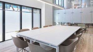 Een moderne vergaderruimte met een grote witte tafel, beige stoelen en grote ramen met uitzicht op het omliggende landschap.