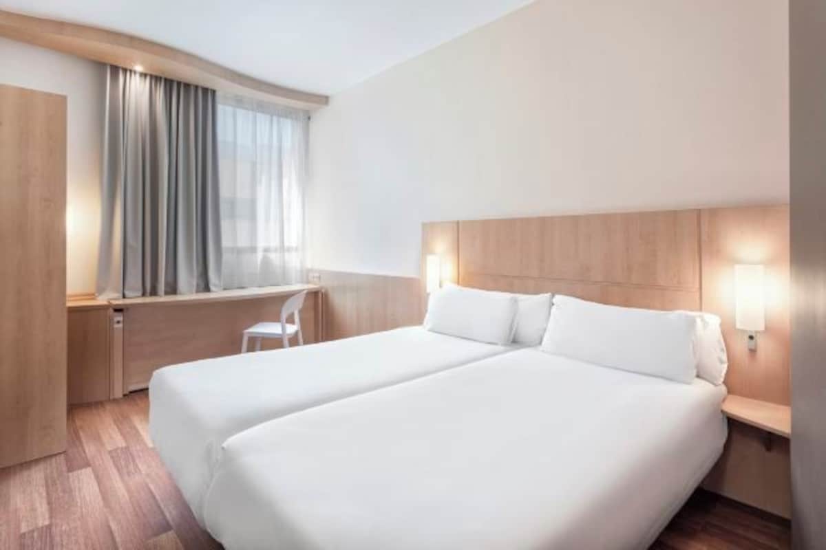 Ett hotellrum med två sängar, ett skrivbord, en stol och ett fönster med gardiner.