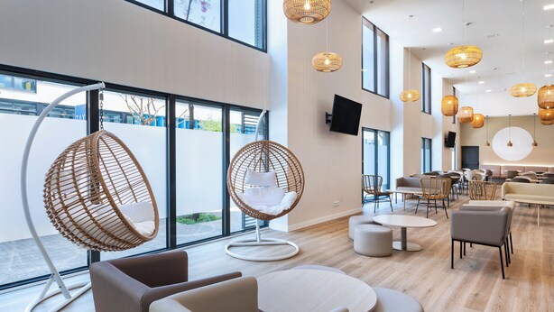 Een modern interieur met rieten stoelen, ronde tafels en een flatscreen televisie aan de muur.