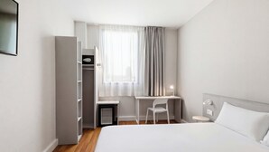 Een hotelkamer met een bed, een bureau, een stoel, een kledingkast en een raam met gordijnen.