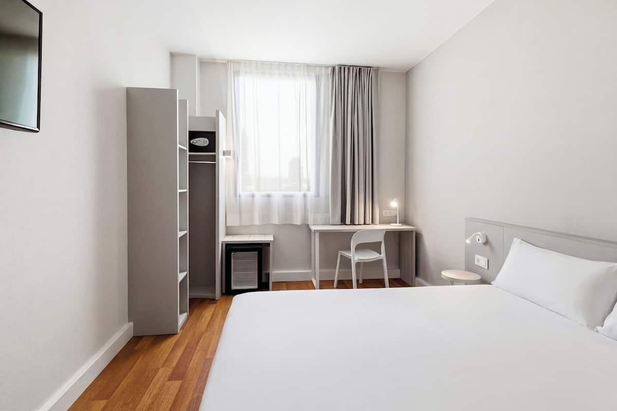 Una camera d'albergo con un letto, una scrivania, una sedia, un armadio e una finestra con tende.