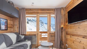 A cozy room with a grey sofa, a small round table, and a TV mounted on the wooden wall.