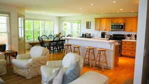 A spacious living area with a dining table and chairs, a kitchen with wooden cabinets and a microwave, and a large window providing natural light.