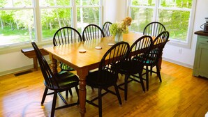 A dining room with a wooden table and black chairs, large windows with a view of greenery, and a vase with flowers on the table.