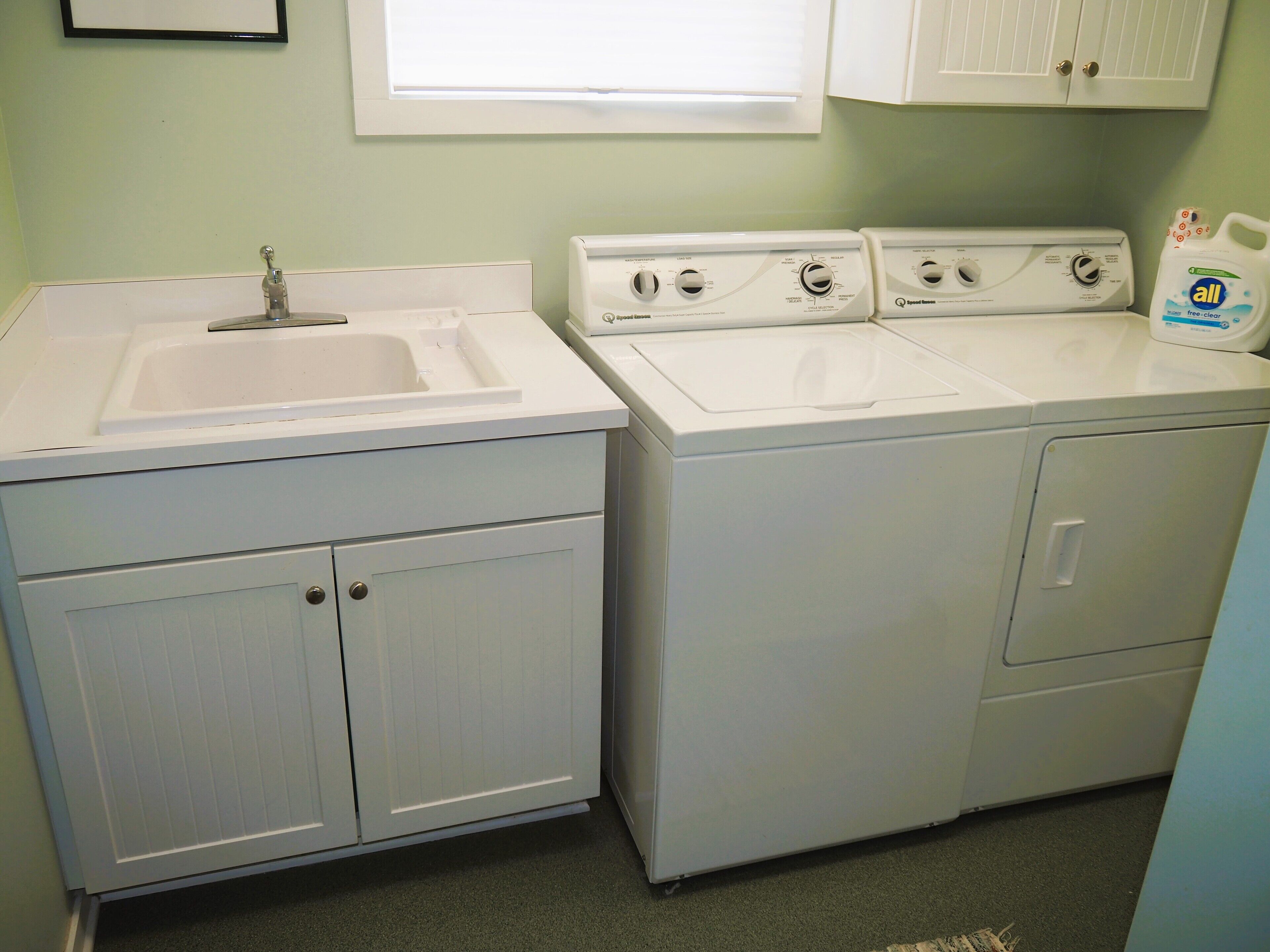 A laundry area with a sink, three stacked washers, and a detergent bottle.