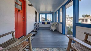 A covered porch with a red door, wooden benches, a seating area with cushions, and large windows. - Turtle Time- Charming 3BR Getaway Near Kure Beach (Kure Beach)